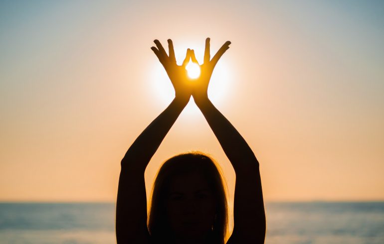 Silhouette of a woman doing yoga on the beach by sunset.