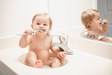 Baby sitting in the wash basin and brushing his teeth.