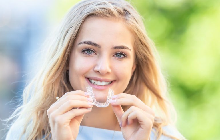 A smiling teenage girl with holding an Invisalign orthodontic tray.