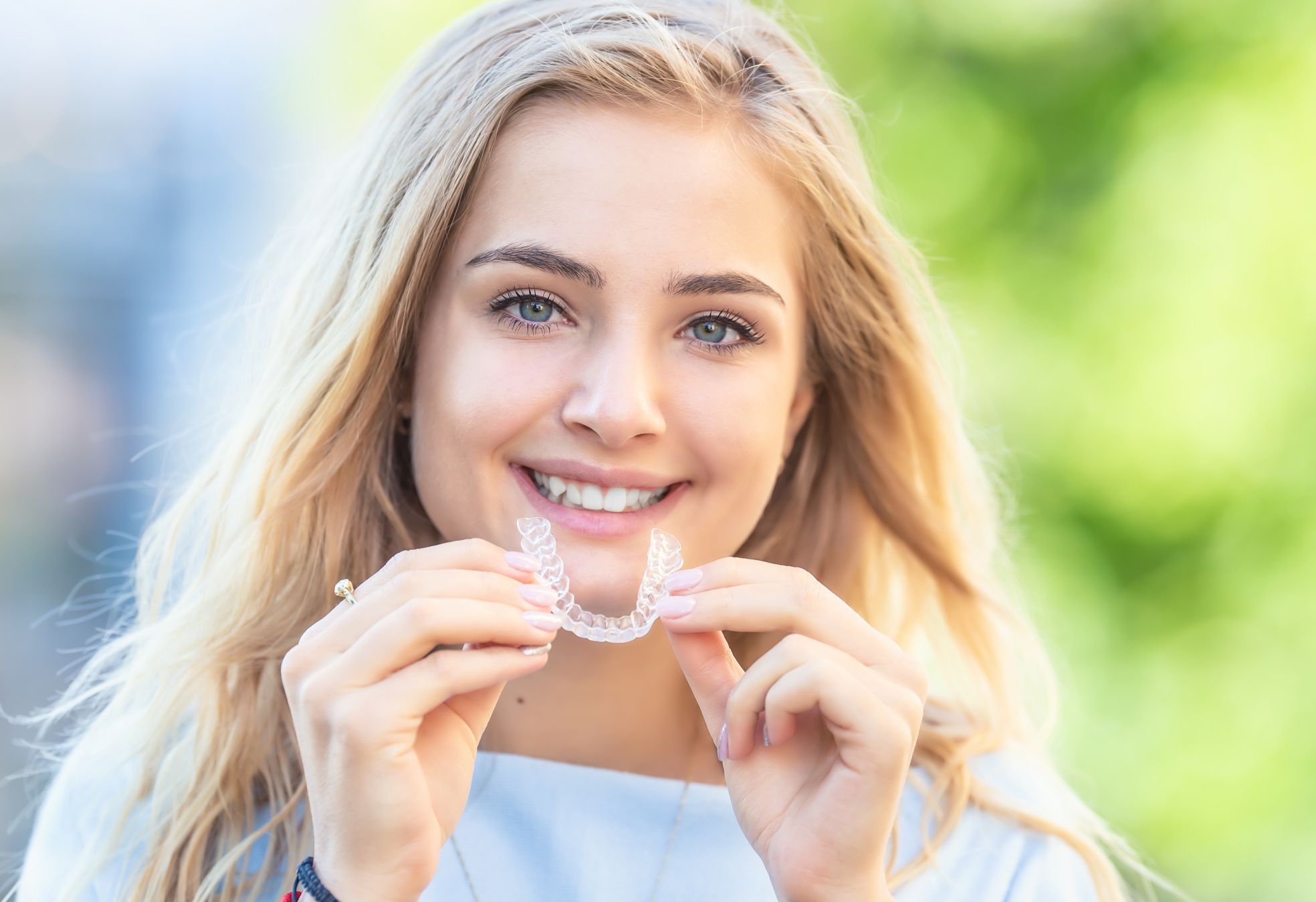 A smiling teenage girl with holding an Invisalign orthodontic tray.
