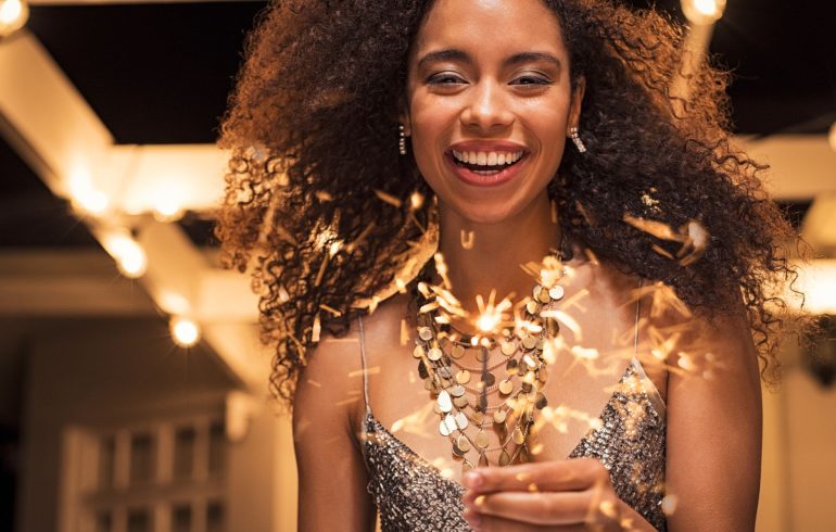 Beautiful Afro-american woman with a perfect smile holding a sparkle stick during New Year's party.