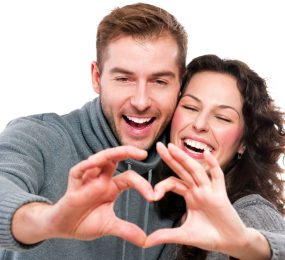 Happy couple with perfect smiles making shape of heart with their hands.