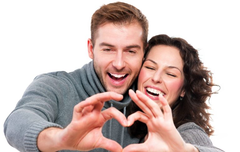 Happy couple with perfect smiles making shape of heart with their hands.