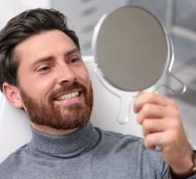 A satisfied man in a dental chair looking at his new dental implants in a mirror