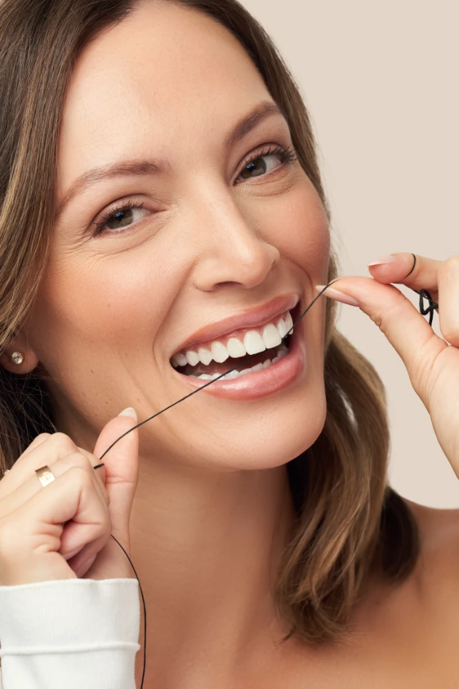 A person smiling while holding dental floss, demonstrating expert flossing technique against a plain background—brought to you by Les Belles NYC Dentistry.