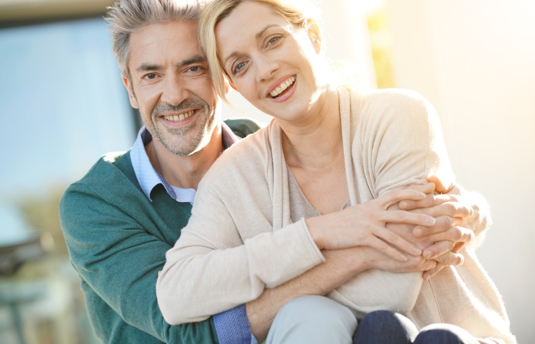 Cheerful middle-aged couple sitting in front of new home
