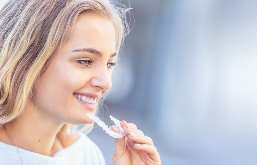 Invisalign orthodontics concept - Young attractive woman holding - using invisible braces or trainer.