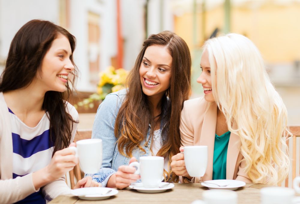 Three beautiful young women with perfect smiles having a chat over a coffee at a cafe