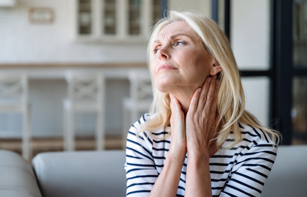 Unhealthy mature woman holding hands on neck, touching lymph nodes. Feeling discomfort, painful sensations, difficult to swallow, throat pain, irritation