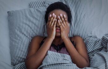 Afro-American woman woken up at night due to sleep apnea symptoms covering her face with hands