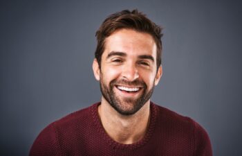 Confidence, face and smile of man in studio, sweater and warm for winter in Canada, happy and discount. Gray background, portrait and joy of person, sale and cardigan of cotton, clothes and jersey