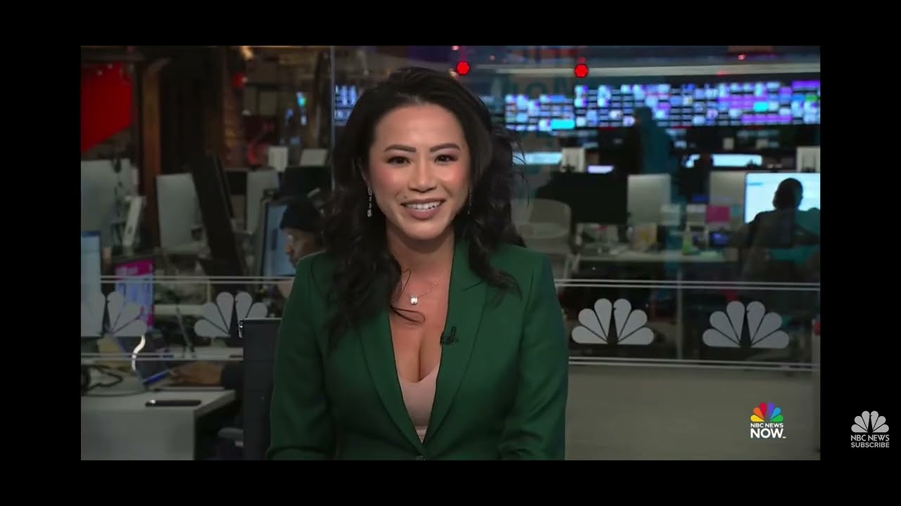 A news anchor wearing a green blazer sits in a newsroom studio, smiling at the camera, with monitors and NBC logos visible in the background.