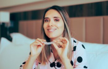 A woman with dental nightguards sitting in bed and getting ready to sleep